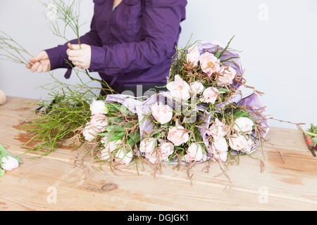 Nahaufnahme eines jungen Floristen arrangieren von Pflanzen und Rosen in Blumenstrauß Stockfoto