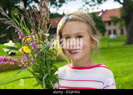 Blonde Mädchen, 6, hält eine Reihe von wilden Blumen vor einem Bauernhaus, Bayern Stockfoto