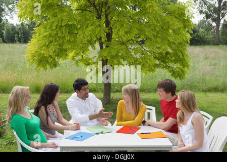 Sechs junge Menschen, die eine Diskussion um einen runden Tisch in einem Garten, Hagen, Niedersachsen Stockfoto