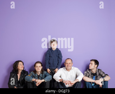 Junge steht in der Mitte sitzt Familie vor lila Hintergrund Stockfoto