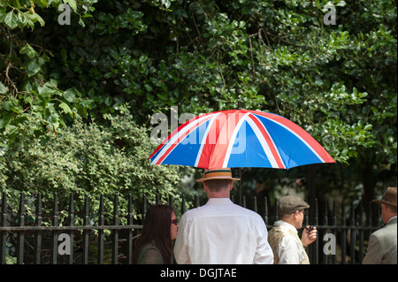 Ein Anschluß-Markierungsfahne Regenschirm statt in die Schlange der wartenden Bedford Square Gardens für den Start der Chap-Olympiade eingeben. Stockfoto