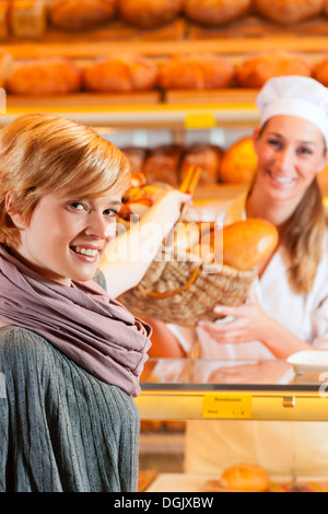 Weibliche Bäcker oder Verkäuferin in ihrer Bäckerei mit einer Kundin und frischem Gebäck oder Backwaren Stockfoto