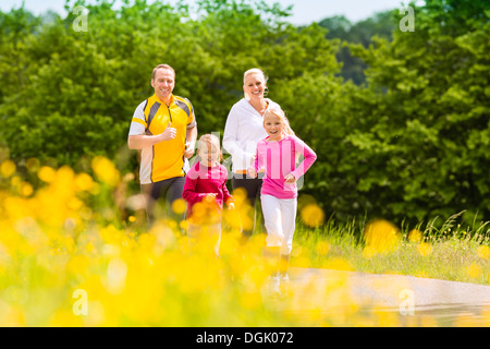 Glückliche Familie mit zwei Mädchen laufen oder Joggen für Sport und besserer Fitness auf einer Wiese im Sommer Stockfoto