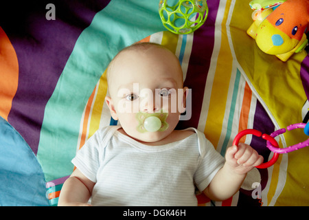 Baby Junge liegend auf Decke Schnuller saugen und spielen mit Spielzeug Stockfoto