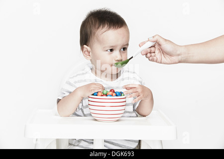 Baby Junge sitzen im Hochstuhl wird spoonfed Stockfoto