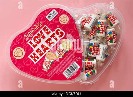 Herzförmige Kunststoffbehälter von Swizzels Matlow Love Hearts Süßigkeiten Bonbons mit Deckel ab, um Inhalte isoliert auf rosa Hintergrund zu zeigen - liebes Herz Stockfoto