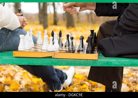 Planung und Strategie in einer Partie Schach Nahaufnahme wie ein Mann seine Hand oben ein Schachbrett mit Figuren wie er eine Entscheidung über seine Macht als nächstes bewegen, schwebt von dem Schachbrett auf einer Parkbank ausgeglichen. Stockfoto