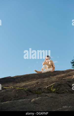 Reife Frau sitzt auf Felsen Stockfoto