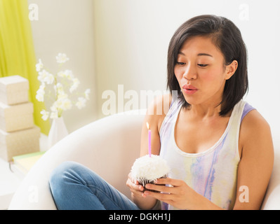 Junge Frau hält Cupcake und Kerze ausblasen Stockfoto