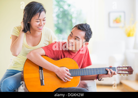 Junger Mann spielt Gitarre, Frau hören Stockfoto