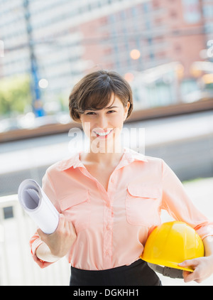 Porträt lächelnde Frau mit Blaupausen und Schutzhelm, Jersey City, New Jersey, USA Stockfoto