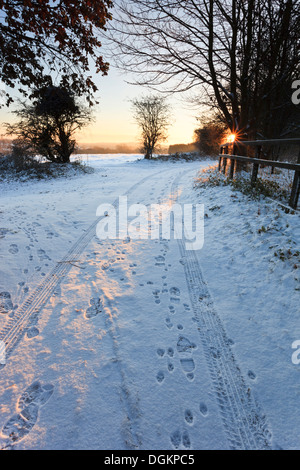 Reifenspuren und Fußspuren im Schnee an einem verschneiten Wintermorgen. Stockfoto