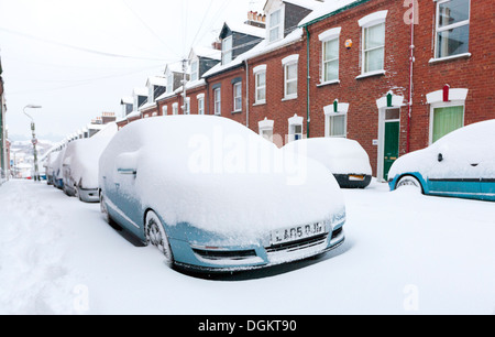 Eine Reihe von Schnee bedeckt entlang einer Straße in Exeter geparkten Autos. Stockfoto