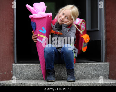 Mädchen, 6 Jahre, mit Schulrucksack und Schule Kegel mit Leckereien für den ersten Tag der Schule Stockfoto