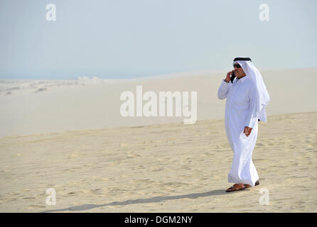 Katar auf einem Handy in der traditionellen Kleidung mit Gutra, Emirat Katar, Persischer Golf, mittleren Osten, Asien Stockfoto