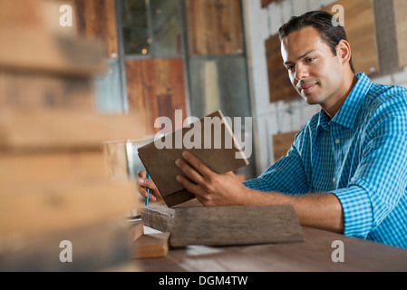 Ein junger Mann in einem Workshop eine recycelte Holz Probe untersuchen. Stockfoto