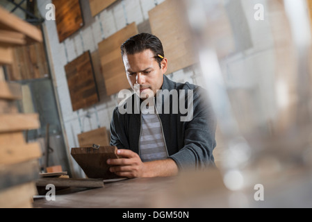 Ein junger Mann in einer Werkstatt, die recycelt und aufgearbeiteten Holz verwendet, um Möbel und Objekte erstellen. Stockfoto