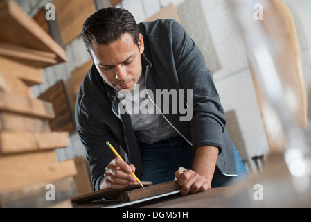 Ein junger Mann in einer Werkstatt, die recycelt und aufgearbeiteten Holz mit Papier und Stift, Aufzeichnungen verwendet. Stockfoto