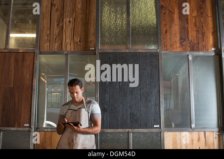 Ein junger Mann in einer Werkstatt. Verwenden eine digitale-Tablette, Aufzeichnungen und Foto-Objekte. Stockfoto