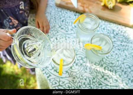 Machen Limonade Overhead Schuss Limonade Gläser frische Zitronenscheibe im Rand des Glas Kind Gießen Drink von Krug. Stockfoto
