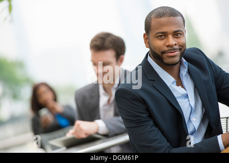 Sommer. Drei Leute, die draußen arbeiten. Mit Hilfe eines digitalen Tablets und Smartphones. Stockfoto