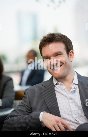 Sommer. Ein junger Mann mit offenem Kragen und Jacke sitzen auf einer Bank. Stockfoto