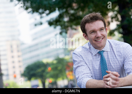 Sommer. Ein Mann in einem weißen Hemd und blaue Krawatte mit seinen Händen umklammert, stützte sich auf ein Geländer. Stockfoto