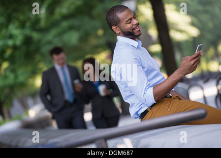 Sommer in der Stadt. Ein junger Mann in einem grauen Anzug und blaue Krawatte zu Fuß mit einer Frau in einem Anzug. Ein Mann sitzt auf einer Bank. Stockfoto