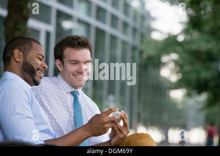 Sommer. Zwei Männer sitzen auf einer Bank mit einem Smartphone. Stockfoto