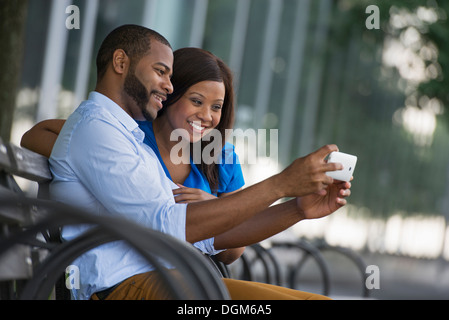 Sommer. Ein paar sitzt auf einer Bank, mit dem selfy fotografieren. Stockfoto