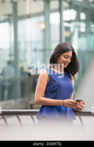 Eine Frau in einem blauen Kleid, überprüfen ihr Smartphone. Stockfoto