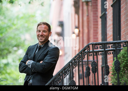 Business-Leute. Ein Mann in einem Anzug auf den Stufen eines Brownstone-Gebäudes. Arme verschränkt. Stockfoto