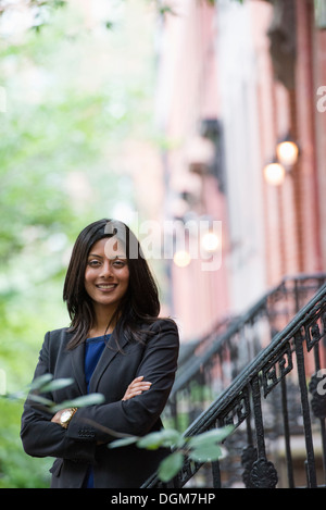 Business-Leute. Eine junge Frau in einem blauen Kleid und grauen Jacke auf Schritte außerhalb eines Gebäudes. Stockfoto