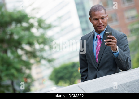 Ein junger Mann in einem Business-Anzug, ein hellblaues Hemd mit roter Krawatte. In einer New-York-City-Straße. Verwenden ein smart Phone. Stockfoto