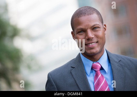 Ein junger Mann in einem Business-Anzug, ein hellblaues Hemd mit roter Krawatte. Auf einer Stadtstraße. Lächelnd in die Kamera. Stockfoto