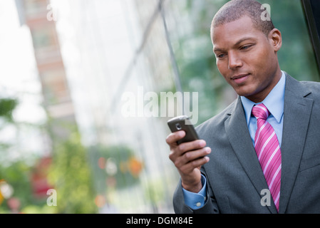 Ein junger Mann in einem Business-Anzug, ein hellblaues Hemd mit roter Krawatte. In einer New-York-City-Straße. Verwenden ein smart Phone. Stockfoto