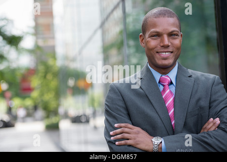 Ein junger Mann in einem Business-Anzug, ein hellblaues Hemd mit roter Krawatte. Auf einer Stadtstraße. Lächelnd in die Kamera. Stockfoto