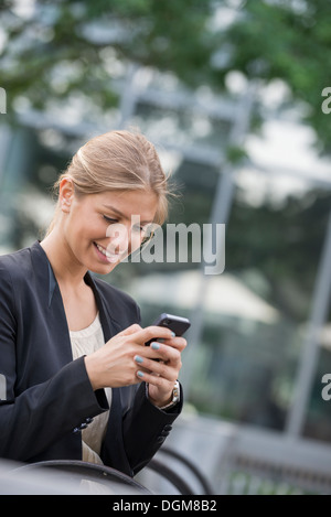 Eine junge blonde Geschäftsfrau in einer New-York-City-Straße. Trug eine schwarze Jacke. Verwenden ein smart Phone. Stockfoto