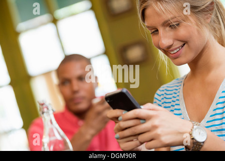 Ein paar in einem Café der Stadt. Eine Frau sitzen Überprüfung ein smart Phone. Ein Mann im Hintergrund. Stockfoto