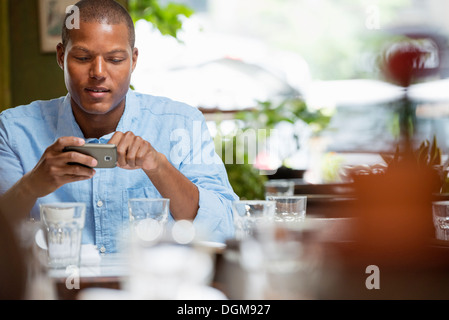 Ein Mann sitzt in einem Stadt-Bistro oder Café durch einen Tisch mit Gläsern und Geschirr. Prüfen seine Telefonnummer. Stockfoto