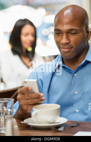 Business-Leute. Zwei Menschen sitzen an Café-Tischen, überprüfen ihre Nachrichten. Stockfoto