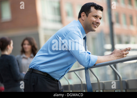 Geschäftsleute im Freien. Ein Latino Geschäftsmann in Hemd und Krawatte, stützte sich auf ein Geländer. Entspannen. Stockfoto