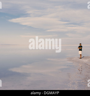 Ein Mann steht am Rand des überfluteten Bonneville Salt Flats in der Abenddämmerung. Arme verschränkt. Stockfoto