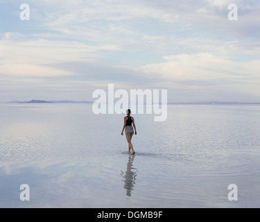 Eine Frau stand auf den überfluteten Bonneville Salt Flats in der Abenddämmerung. Reflexionen im seichten Wasser. Stockfoto