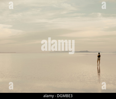 Eine Frau stand auf den überfluteten Bonneville Salt Flats in der Abenddämmerung. Reflexionen im seichten Wasser. Stockfoto