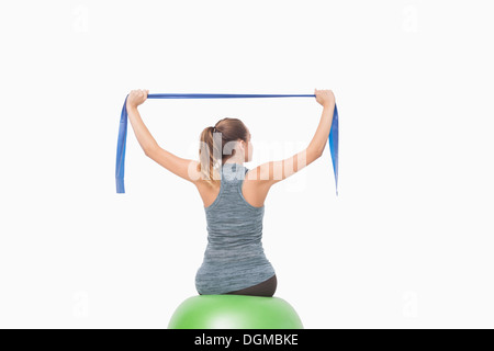 Blonde Frau sitzt auf einer Kugel Fitnesstraining mit einem Widerstand band Stockfoto