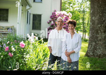 Bio-Bauernhof. Sommer-Party. Ein älteres Paar in weißen Hemden, die unter den Blumen zusammenstehen. Stockfoto