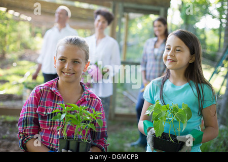 Bio-Bauernhof. Sommer-Party. Zwei Mädchen sitzen halten Jungpflanzen mit ein älteres Paar und eine junge Frau auf der Suche auf. Stockfoto