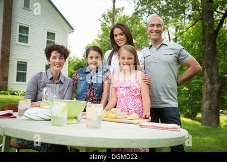 Ein Sommer-Familientreffen auf einem Bauernhof. Fünf Menschen posieren neben dem Tisch, wo ein Kind frische Limonade macht. Stockfoto