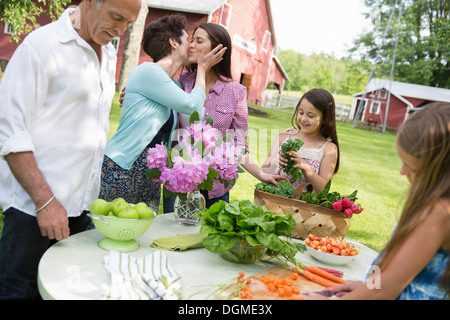 Familienfest. Ein Tisch gedeckt mit Salaten und frischem Obst und Gemüse. Eine Mutter, eine Tochter auf die Wange küssen. Stockfoto